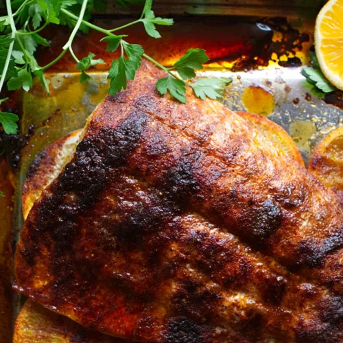 A large Spanish-style Spicy salmon fillet cooked next to slices of orange and fresh parsley.