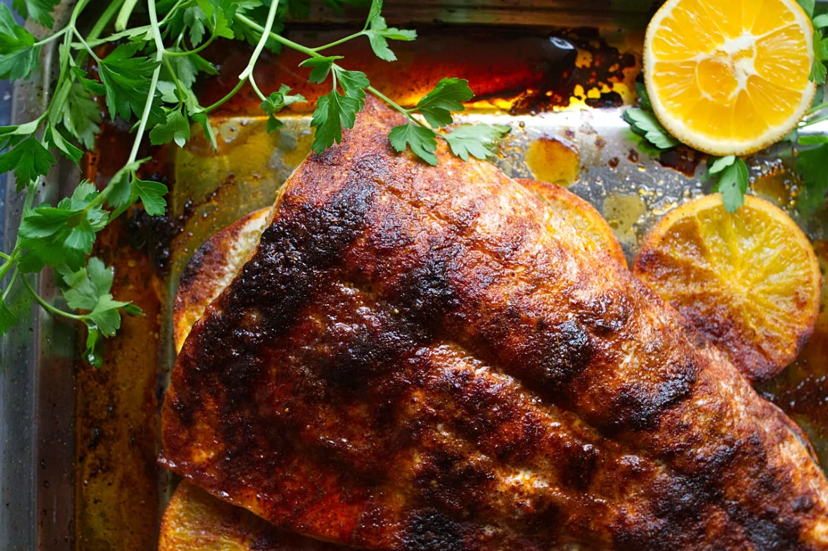 A large Spanish-style Spicy salmon fillet cooked next to slices of orange and fresh parsley.