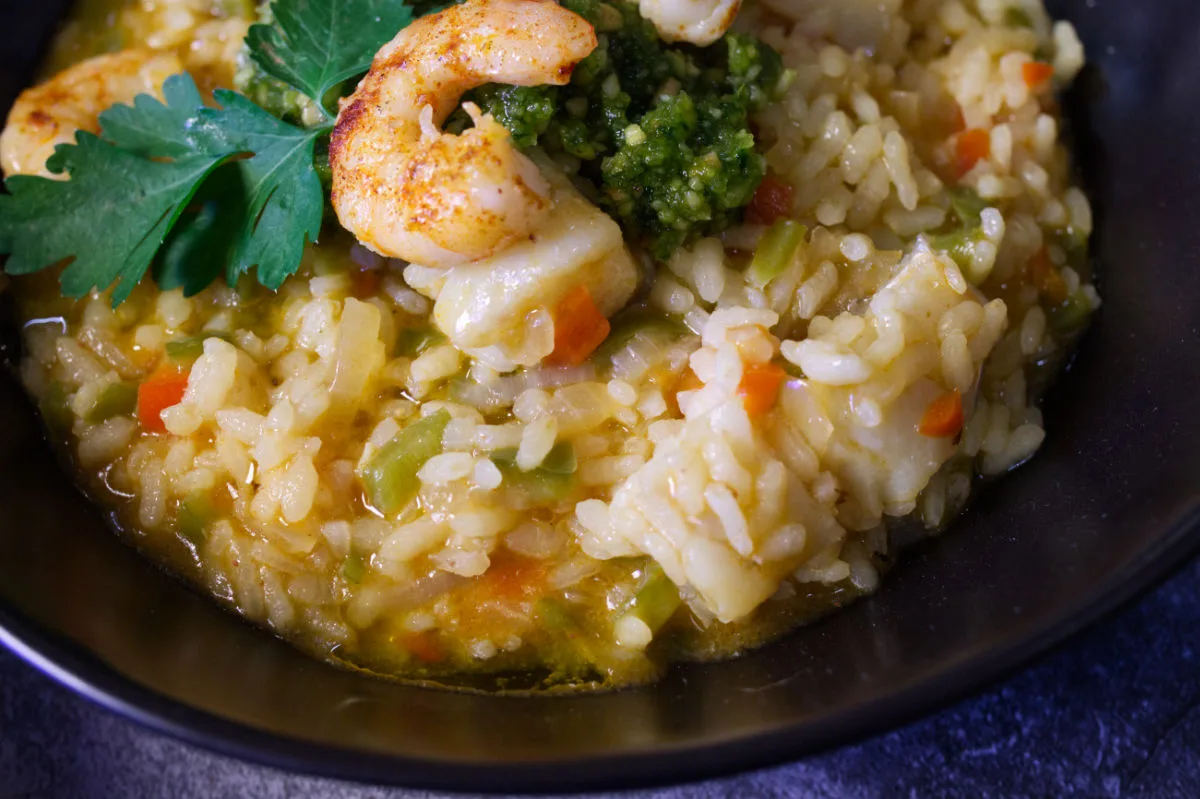 A bowl of brothy fish stew topped with some almond pesto and pan-fried shrimp.