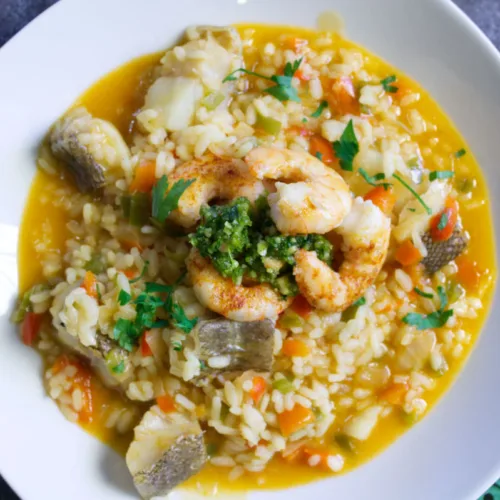 A bowl of brothy fish stew topped with some almond pesto and pan-fried shrimp.