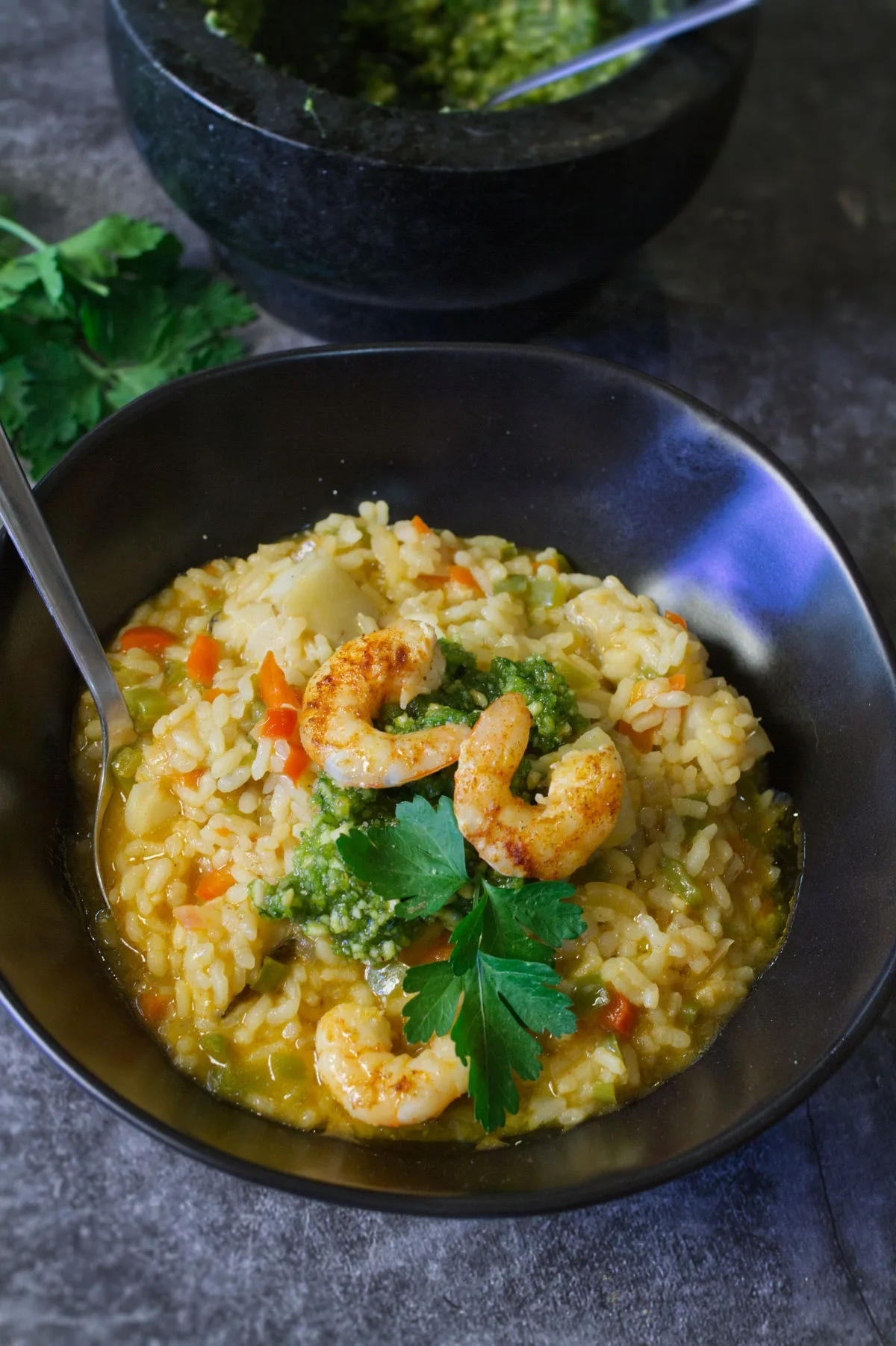 A bowl of brothy fish stew topped with some almond pesto and pan-fried shrimp.