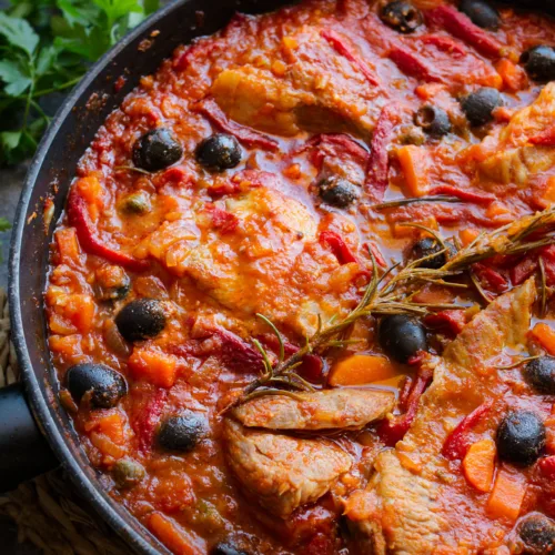 A large pan of Spanish pork secreto garnished with fresh roasemary and black olives.