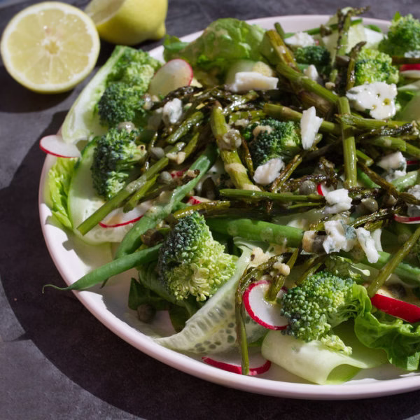 A plate of Spanish Green salad sits beside some fresh lemon.