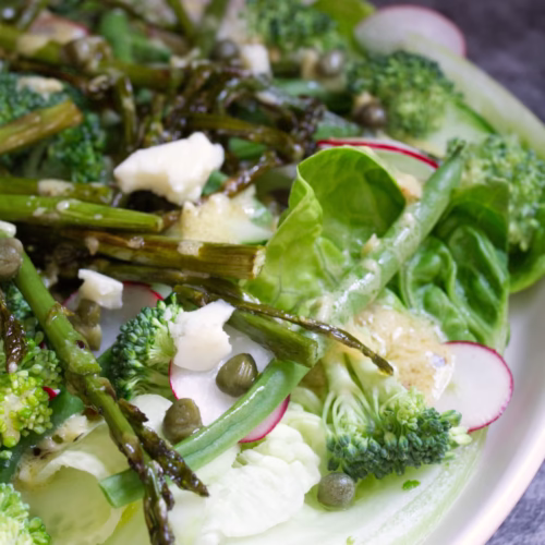 A plate of Spanish Green salad sits beside some fresh lemon.