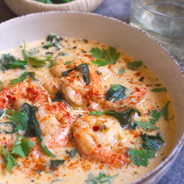 A bowl of creamy shrim soup with spinach and chickpeas is garnished with some fresh parsley