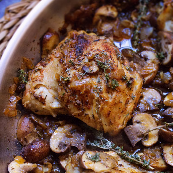 A pan of garlic mushroom chicken thighs with fresh thyme garnish