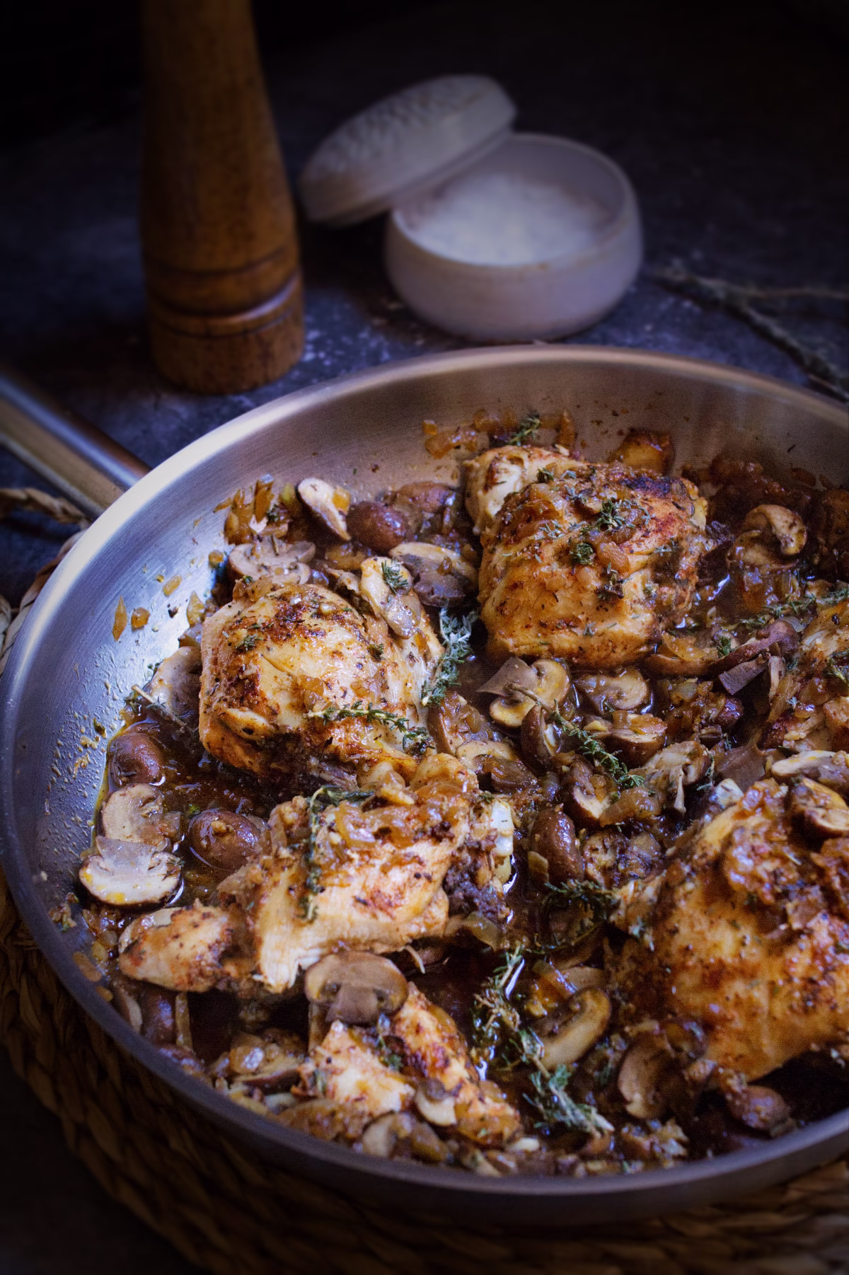 A pan of garlic mushroom chicken thighs with fresh thyme garnish