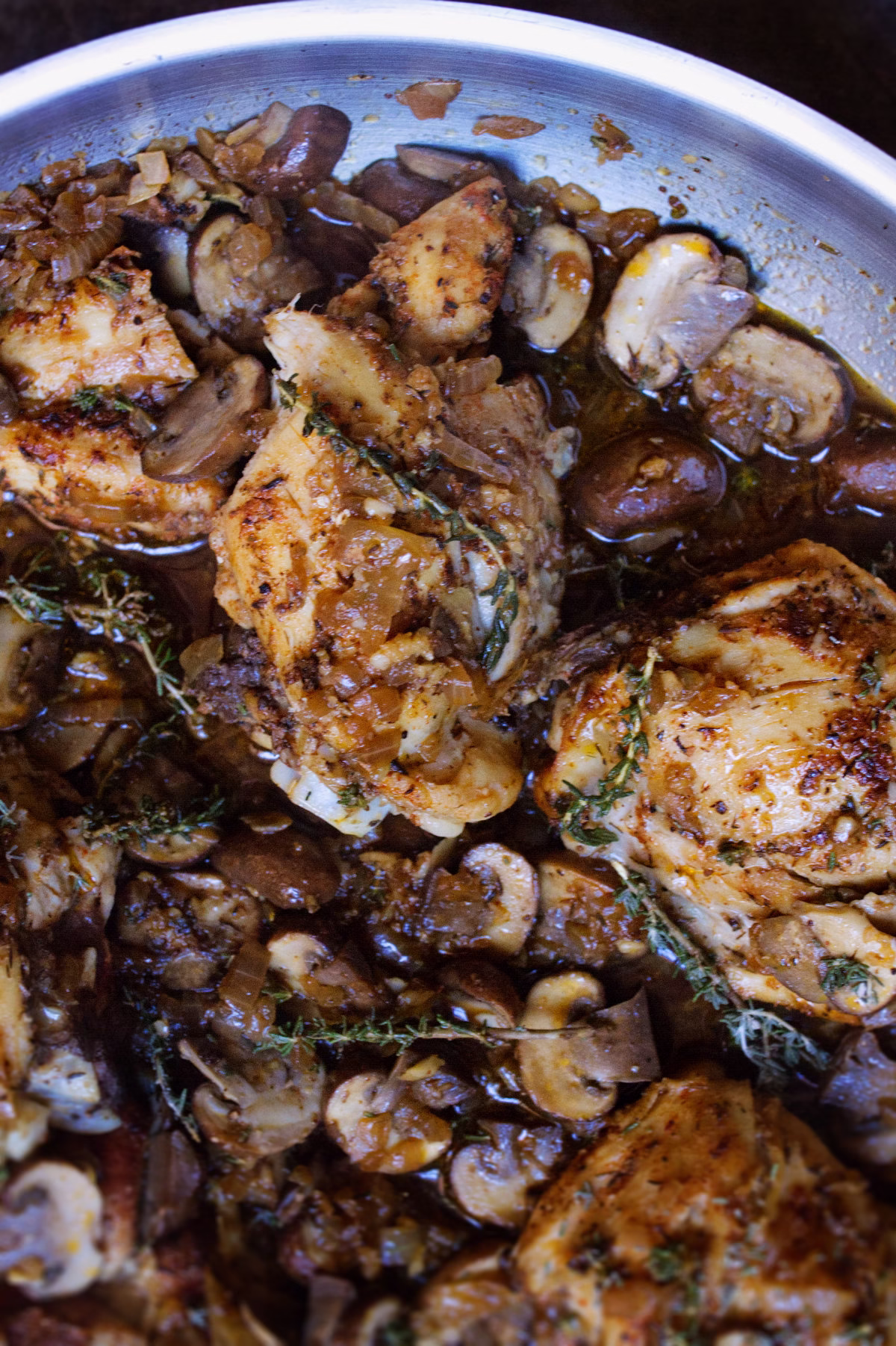 A pan of garlic mushroom chicken thighs with fresh thyme garnish