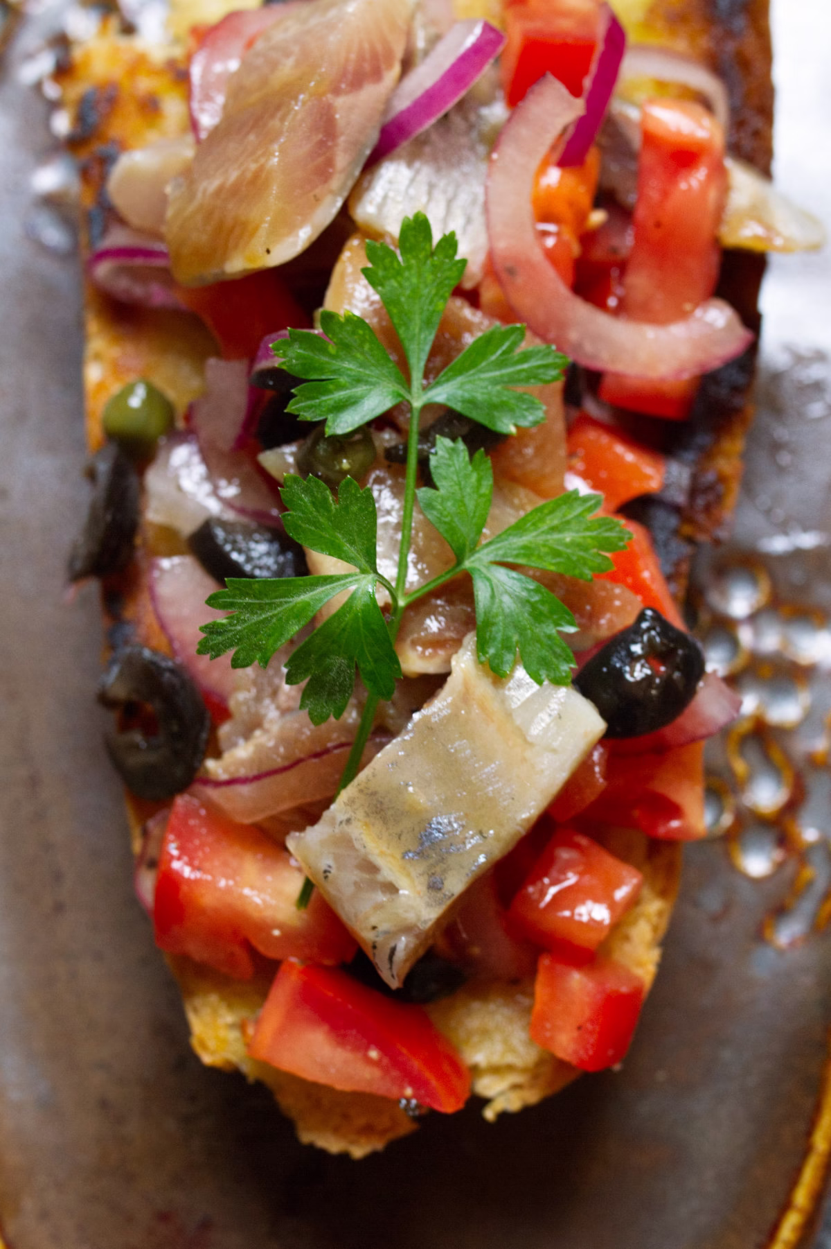 A slice of toast topped with tomato and sardiens with capers and olives