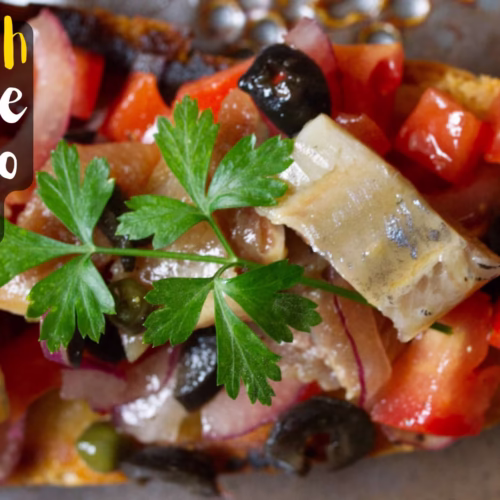 A slice of toast topped with tomato and sardiens with capers and olives