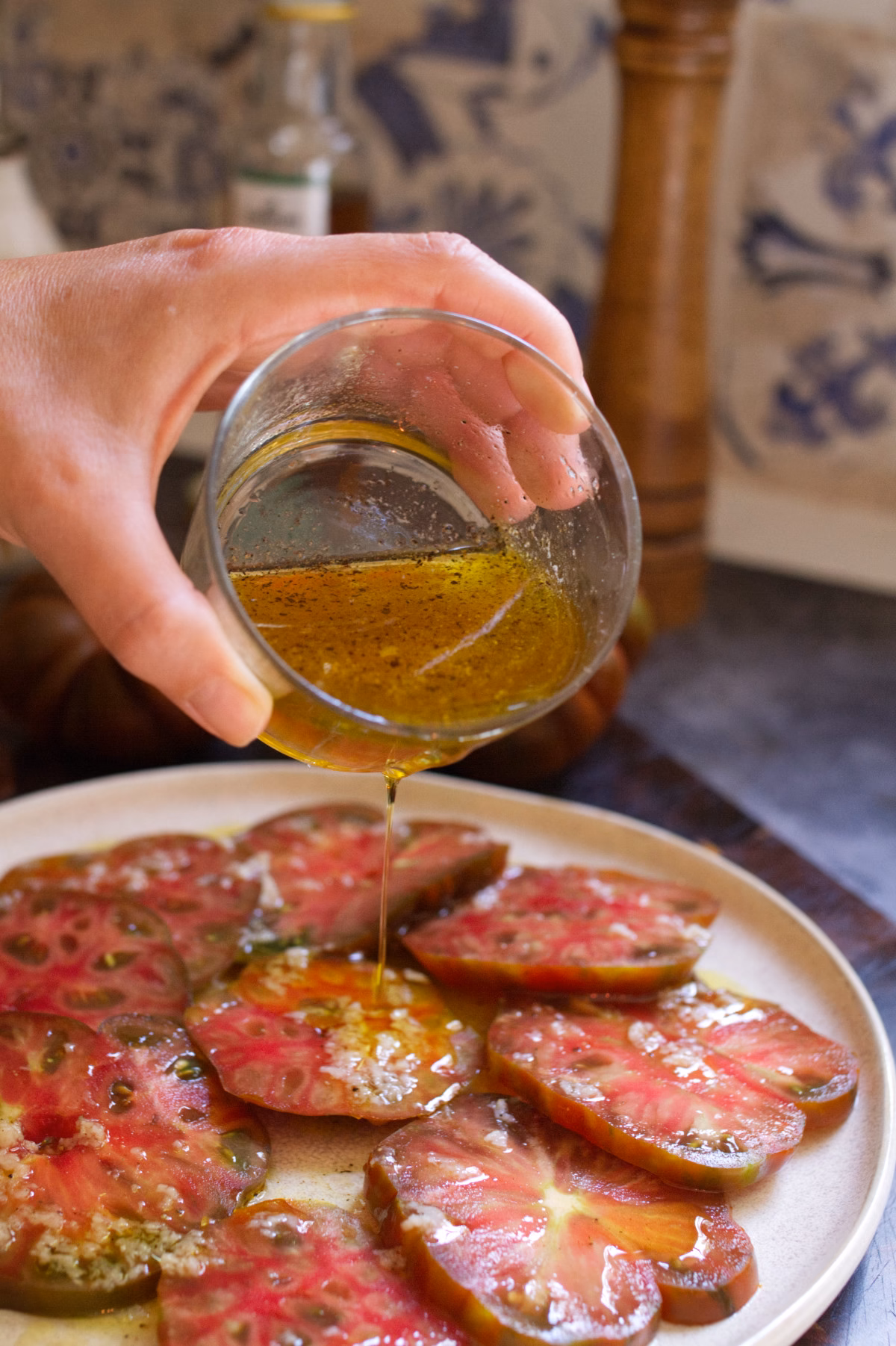 A person drizzles Andalusian Tomato salad dressing over a tomato salad.