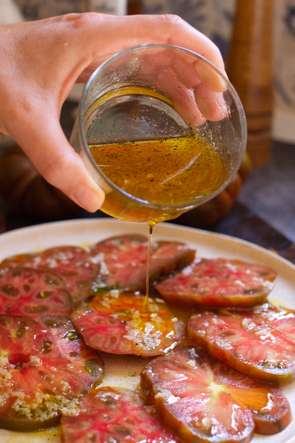 A person drizzles Andalusian Tomato salad dressing over a tomato salad.