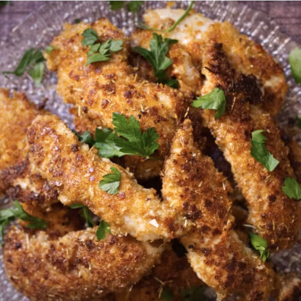 A glass plate serving plate with pieces of crispy chicken tenders on it and a sprinkling of parsley.
