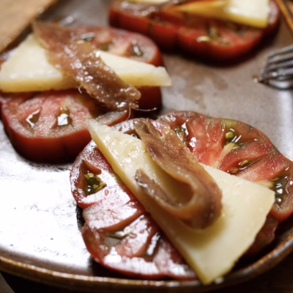 A serving plate with slices of tomato with manchego cheese and an anchovy on each one.