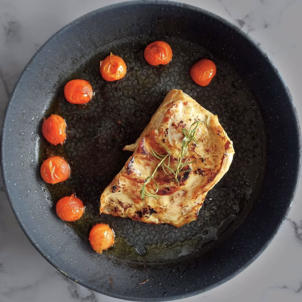 Pork shoulder cooked on a pan surrounded by cherry tomatoes.