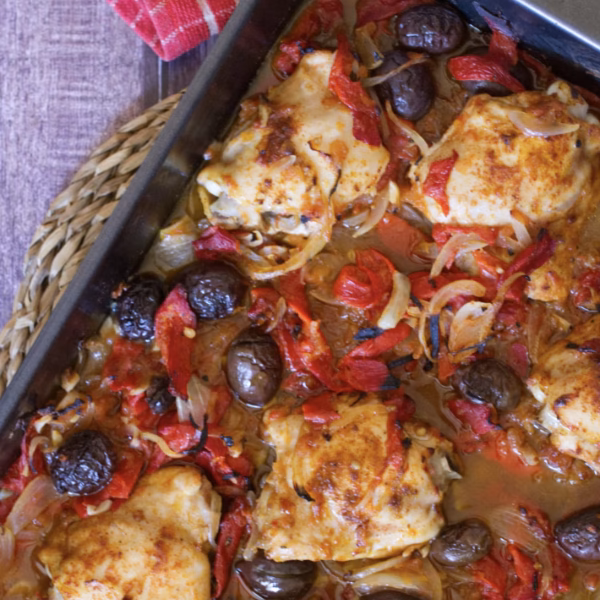 Baked chicken thighs with roasted peppers and black olives scattered around a sheet pan.