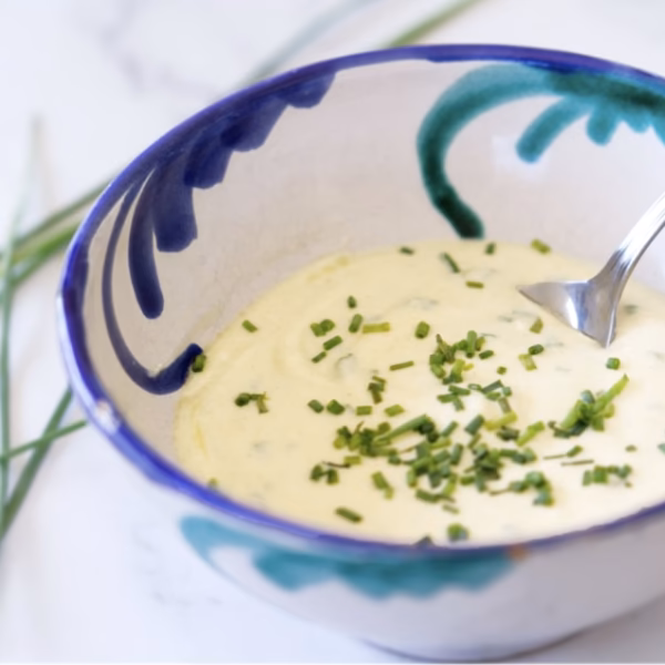 A bowl with yogurt salad dressing in it with some chopped chives on top.