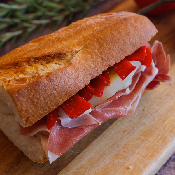 A serrano ham sandwich on a chopping board with cheese and red pepper slices visible.