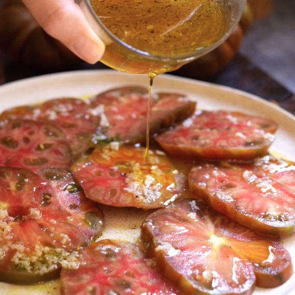 Salad dressing being poured over freshly cut tomatoes.