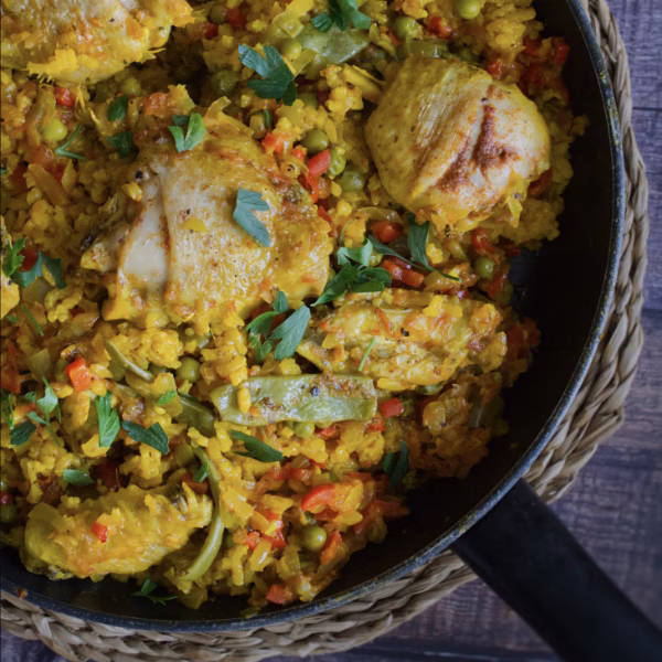 A pan with cooked chicken, rice, and vegetables. The rice has a yellow hue from the saffron.