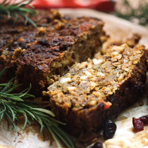 Vegetarian nut roast cut into slices with dried cranberries and rosemary sprigs around them.