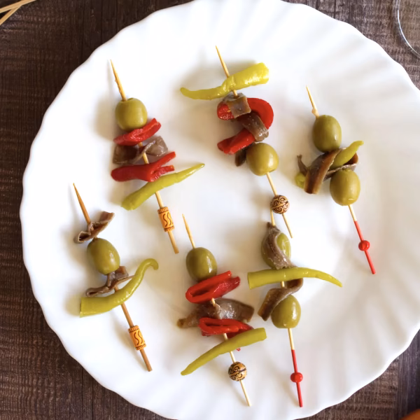 A white plate with six Spanish banderillas laying on top.