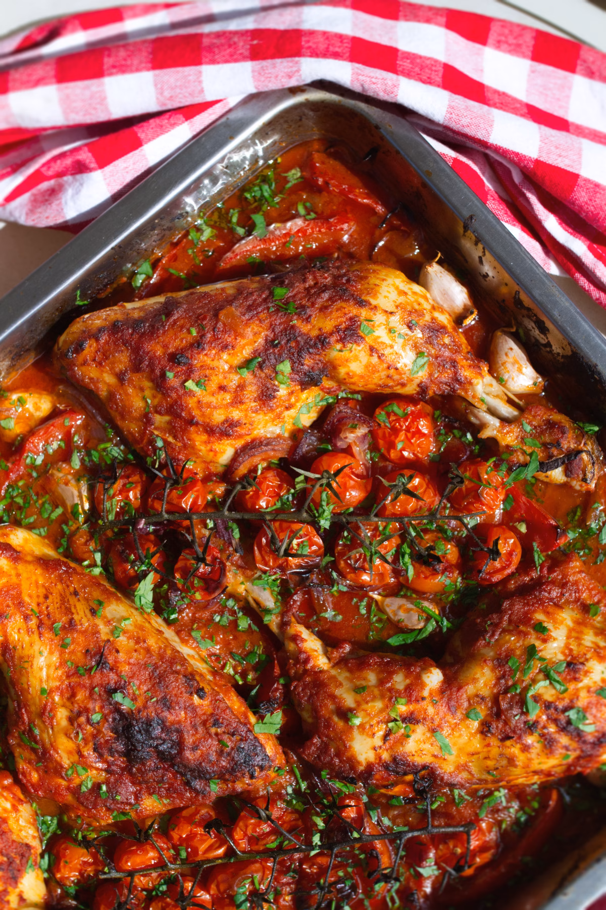 A large pan of Spanish paprika chicken with crispy chicken skin, tomatoes, and onions