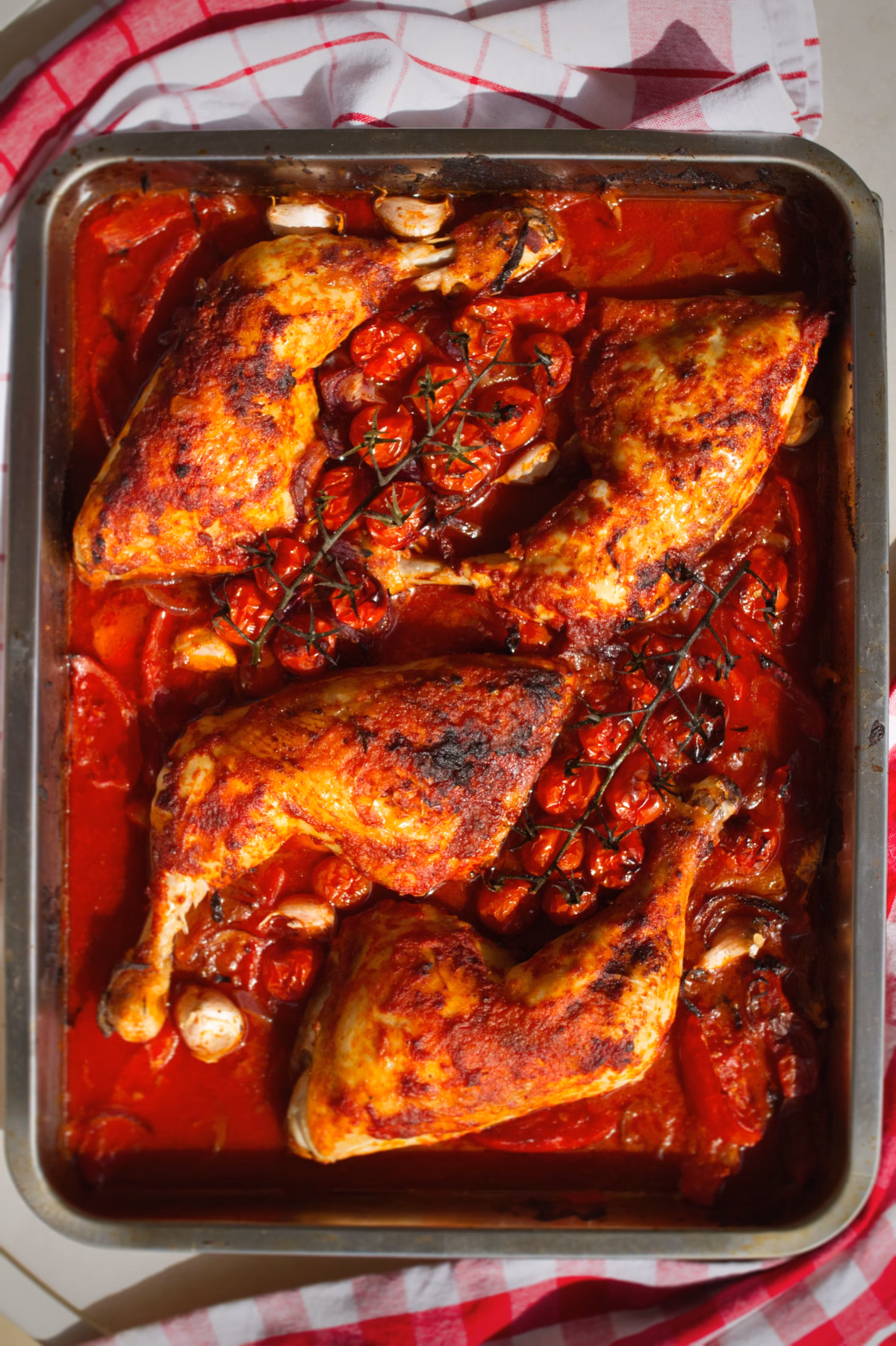 A large pan of Spanish paprika chicken with crispy chicken skin, tomatoes, and onions