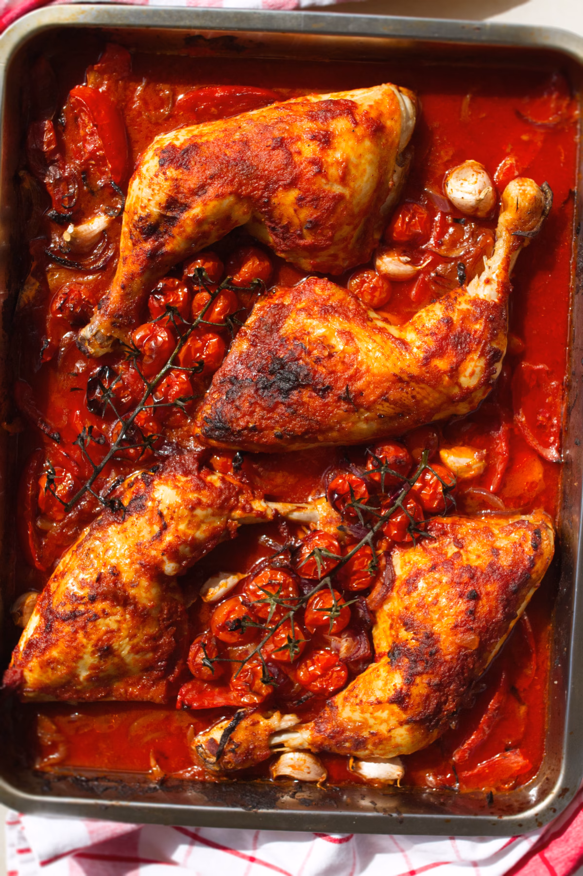A large pan of Spanish paprika chicken with crispy chicken skin, tomatoes, and onions