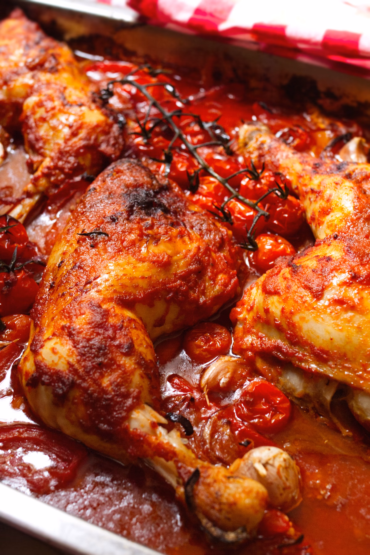 Roasted chicken pieces with crispy skin in a tomato-herb sauce on a baking tray