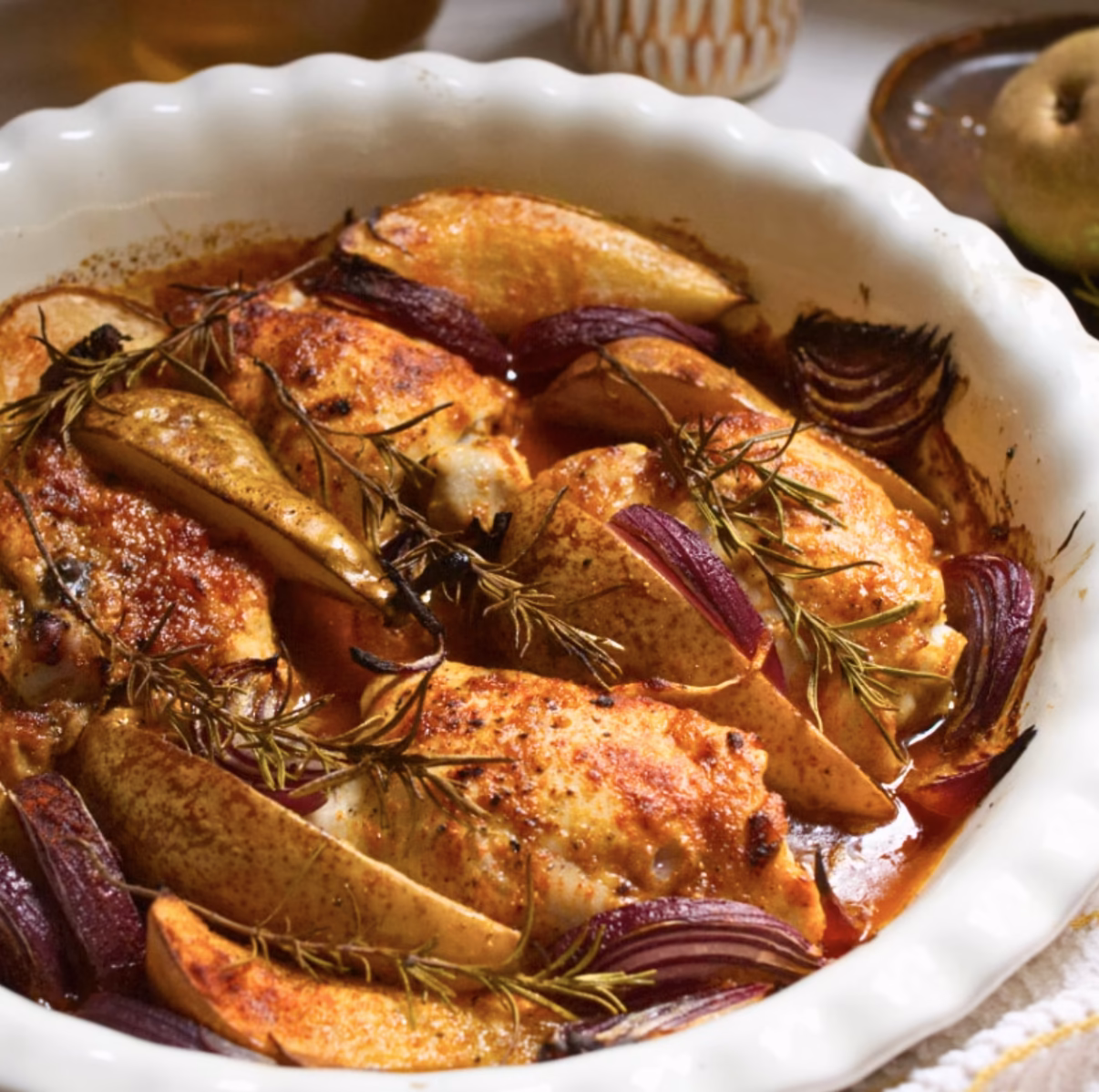 A white casserole dish with baked chicken thighs and spiced pears ready for serving.