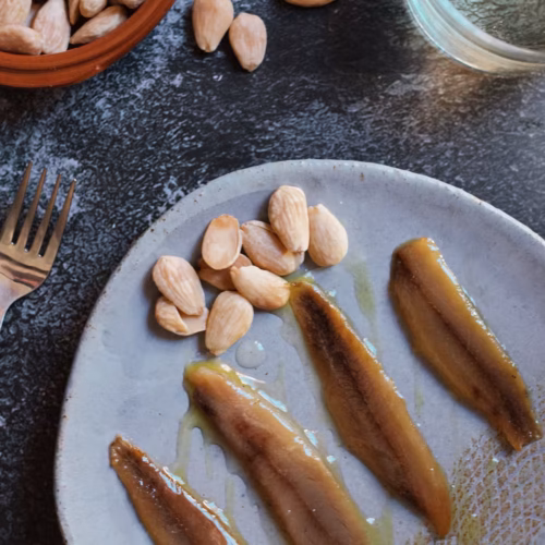 A plate with smoked sardine fillets and toasted almonds above them.