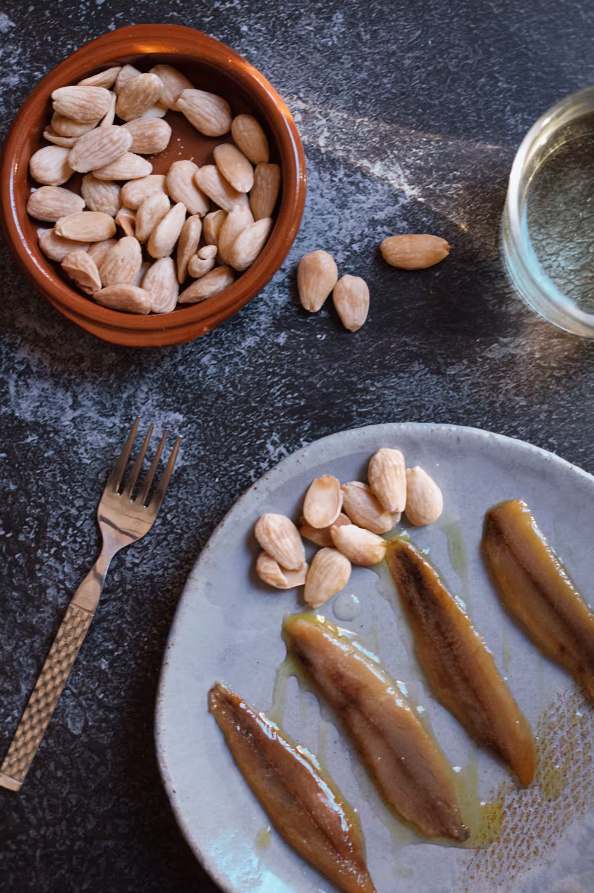 A small dish with toasted almonds in it and a larger dish to the bottom with almonds and four pieces of smoked sardines.