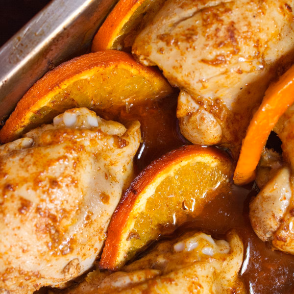 A pan of Spanish oven chicken with sliced orange rounds